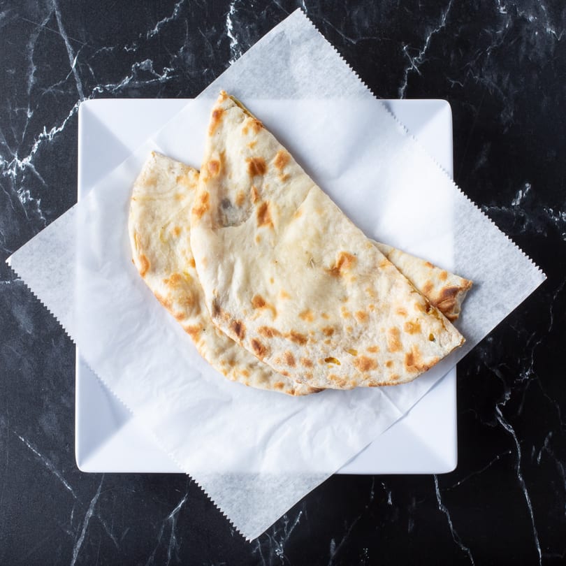 Two pieces of golden-brown naan bread on white parchment paper, served on a square white plate.