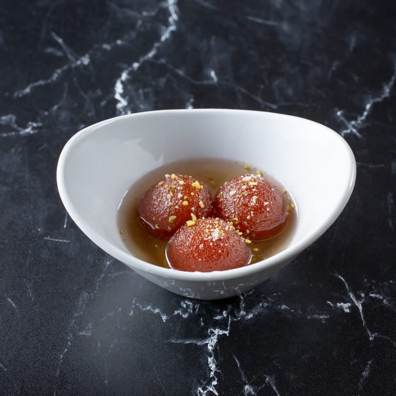 Three Gulab Jamun, Indian fried dough balls in syrup, garnished with nuts in a white bowl.