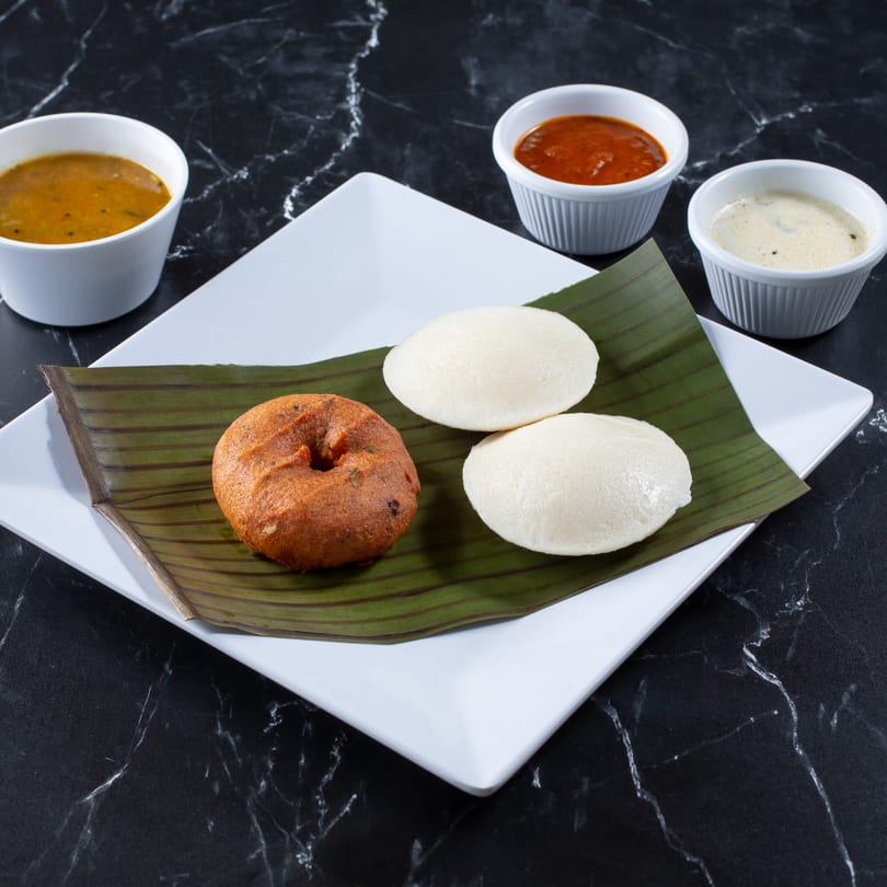 Tulsi Kitchen's vada and idli on a banana leaf, with sambar and chutneys on a black marble surface.