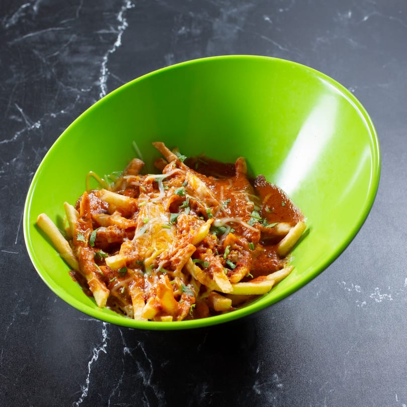 Tulsi Kitchen's chili cheese fries, topped with cilantro, served in a vibrant green bowl.